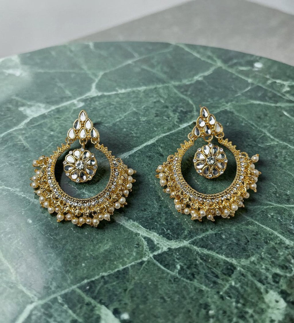 Pair of gold and pearl earrings on a green marble surface