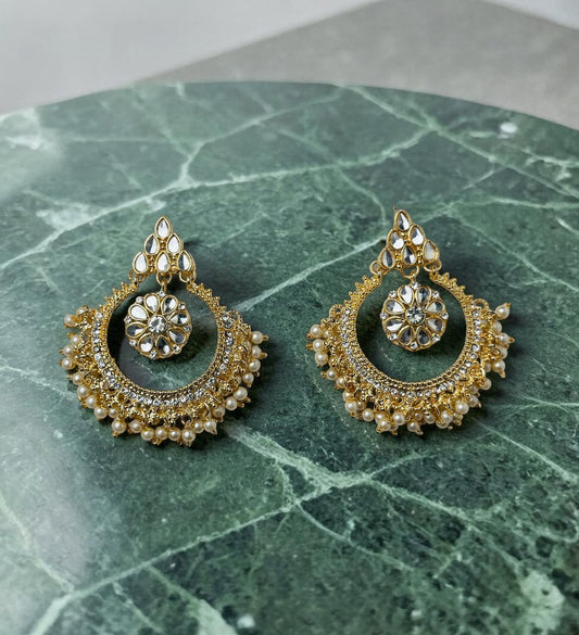Pair of gold and pearl earrings on a green marble surface