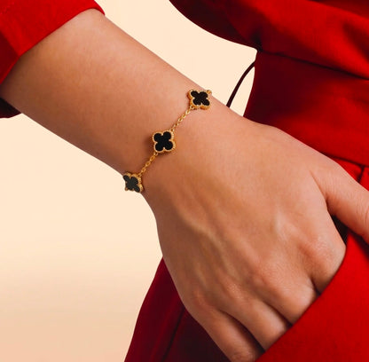 Gold bracelet with black clover-shaped charms on a wrist against a red garment.